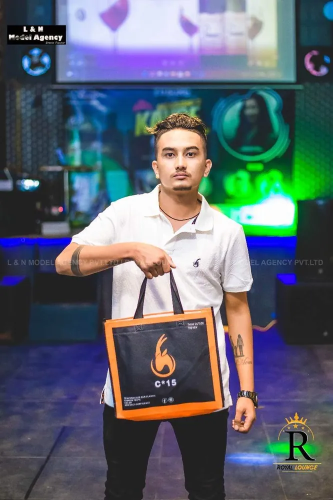 Man in a white polo holding the C-15 tote bag on stage at an evening event