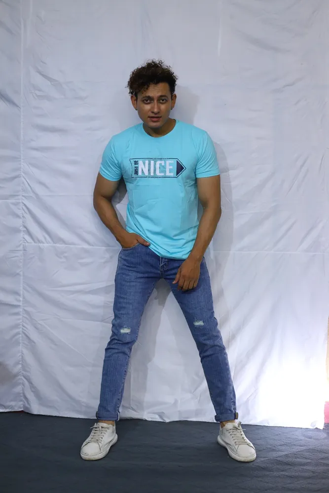 Model standing against a white studio backdrop in a turquoise C-15 tee and ripped light-wash jeans
