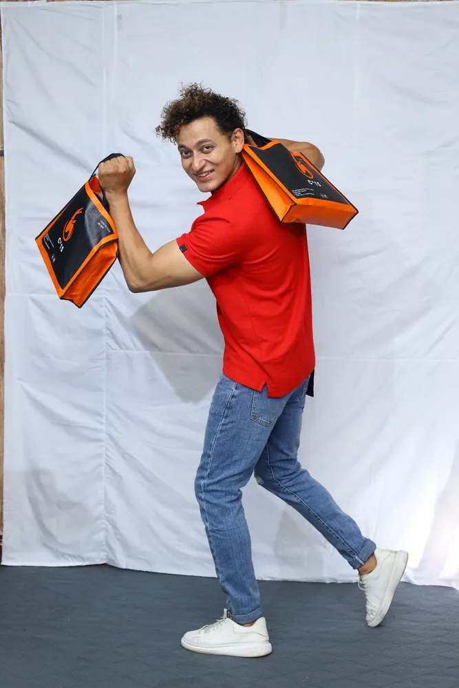 Model in a red C-15 polo and light jeans swinging the orange C-15 tote bag in the studio