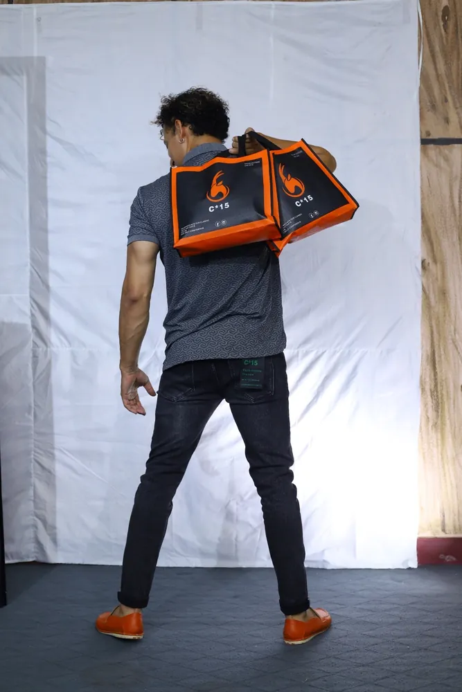 Model from behind with the orange C-15 tote over his shoulder and orange shoes, white studio backdrop
