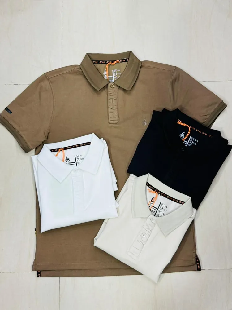 Tan C-15 polo shirt laid out with folded white, black and navy polos on tile