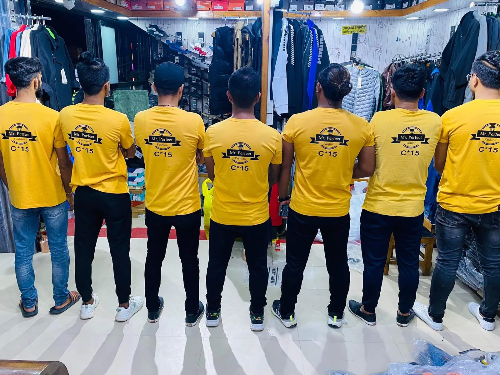 The C-15 team in yellow brand t-shirts standing together inside the shop, racks of menswear around them